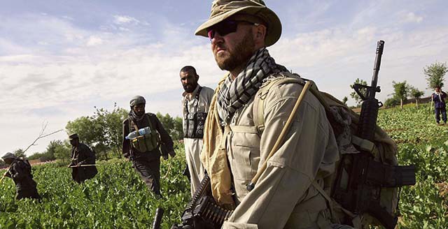 LASHKAR GAH, AFGHANISTAN - APRIL 03:  An American supervisor from the DynCorp security contractor watches Afghan forces cut opium poppies on April 3, 2006 near Lashkar Gah in the Helmand province of southern Afghanistan. Afghan forces are feverishly working to eradicate the poppy fields before the harvest begins in the next month. The Taliban reaps huge profits from protecting the opium trade, according to Afghan officials. Afghanistan produces up to 85 percent of the world's opium and Helmand province almost half of that.  (Photo by John Moore/Getty Images)